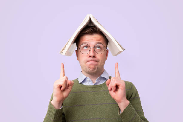 istock Handsome man in glasses holding a bookc on head and pointing up 1187152703