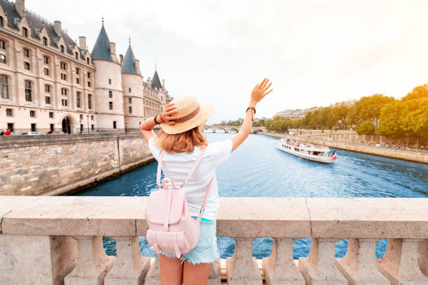 um turista da menina em um chapéu que está em uma ponte e que acena a um cruzeiro do rio que navega pelo rio de sena em paris - paris france panoramic seine river bridge - fotografias e filmes do acervo