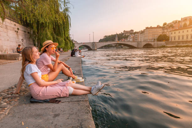 two happy caucasian and asian girls friends meeting great sunset on a river saone in lyon city. travel and lifestyle in france - bridge people fun river imagens e fotografias de stock