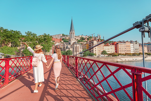Two happy girls friends walking on Saint Georges pedestrian bridge while traveling in Lyon old town in France