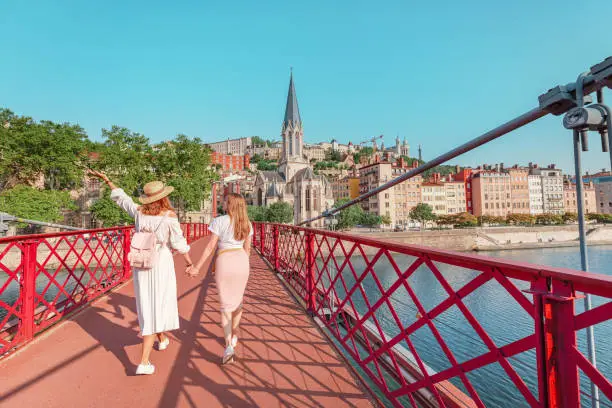 Photo of Two happy girls friends walking on Saint Georges pedestrian bridge while traveling in Lyon old town in France