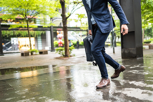 Unrecognizable businessman running to work, low angle view of his pants and shoes on wet city street