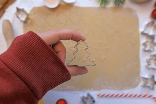 vista superior de la mano sosteniendo cortador de galletas en forma de un árbol de navidad en frente de la masa de galletas enrollada en fondo borroso - candy cane christmas cookie raw food fotografías e imágenes de stock