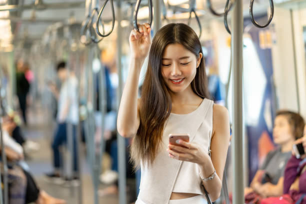 joven asiática pasajera usando la red social a través del teléfono móvil inteligente - bangkok mass transit system fotografías e imágenes de stock