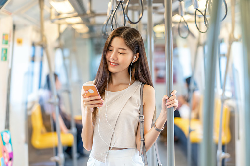 Young Asian woman passenger listening music via smart mobile phone in subway train when traveling in big city
