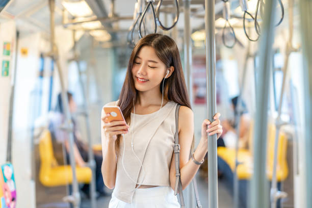 Young Asian woman passenger listening music via smart mobile phone in subway train stock photo