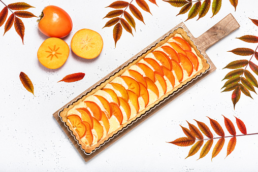 Homemade cake with persimmon and cream cheese in baking dish on the wooden cutting board. Sweet food concept. Flat lay.