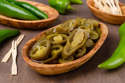 Slices of green pepper pickles in a bowl on a wooden background. Selective focus.