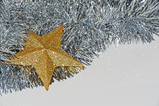 Golden Christmas star and silver tinsel lying on white background