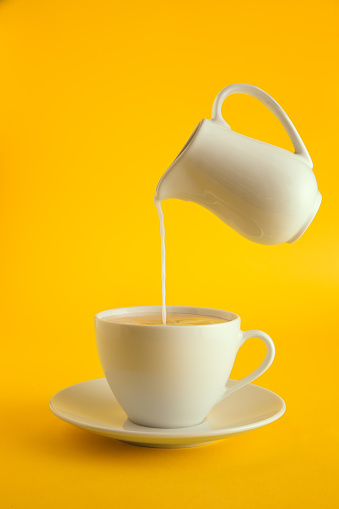 Pouring milk into coffee on yellow background