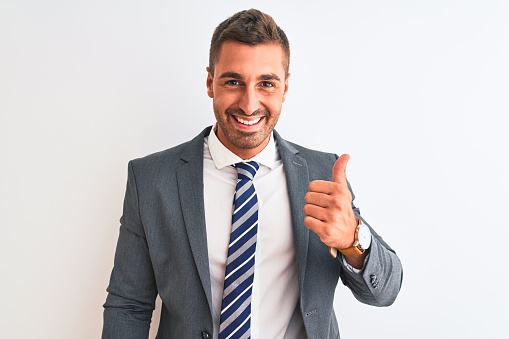 Young handsome business man wearing suit and tie over isolated background doing happy thumbs up gesture with hand. Approving expression looking at the camera showing success.