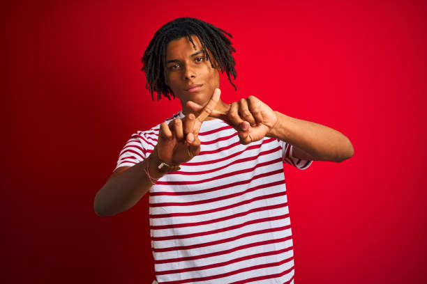 istock Young afro man with dreadlocks wearing striped t-shirt standing over isolated red background Rejection expression crossing fingers doing negative sign 1187190868