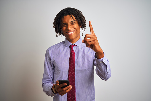 Afro american businessman with dreadlocks using smartphone over isolated white background surprised with an idea or question pointing finger with happy face, number one