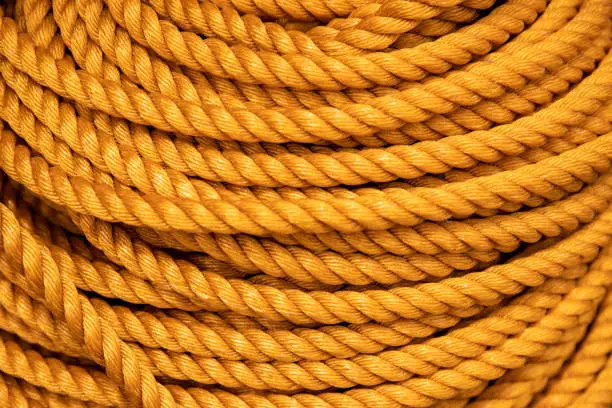 Yellow rope pile closeup photo. Ship or rock climbing tackle. Natural material woven cordage. Simple rope bulk concept. Alpine mountaineering equipment. Safety rope texture. Yacht tackle bundle card