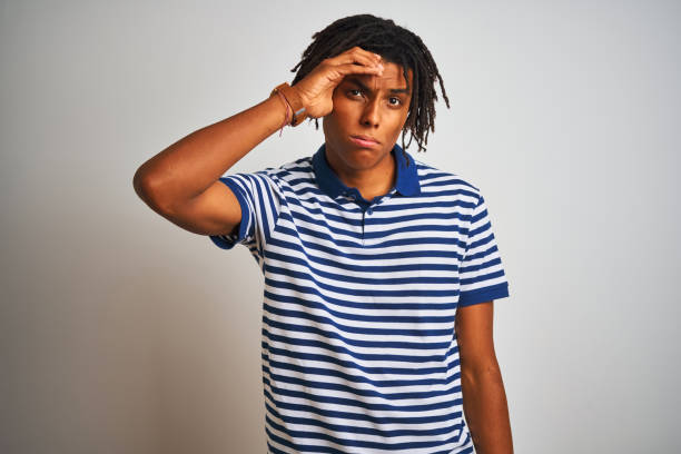 istock Afro man with dreadlocks wearing striped blue polo standing over isolated white background worried and stressed about a problem with hand on forehead, nervous and anxious for crisis 1187191275