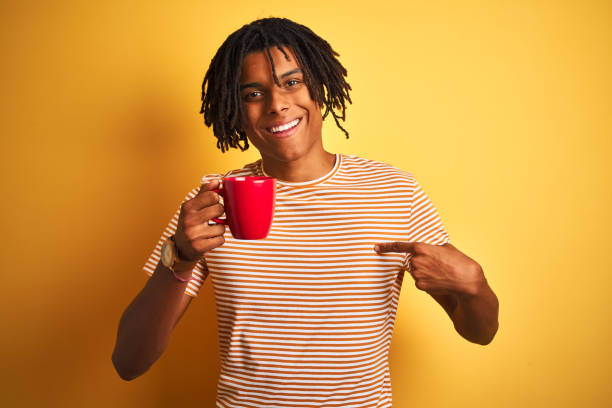 istock Afro american man with dreadlocks drinking a cup of coffee over isolated yellow background with surprise face pointing finger to himself 1187192332