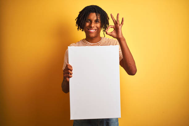istock Afro american man with dreadlocks holding banner over isolated yellow background doing ok sign with fingers, excellent symbol 1187192401
