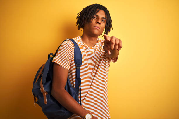 istock Afro american student man with dreadlocks wearing backpack over isolated yellow background pointing with finger to the camera and to you, hand sign, positive and confident gesture from the front 1187192532