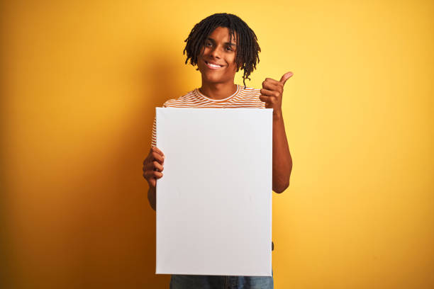 istock Afro american man with dreadlocks holding banner over isolated yellow background happy with big smile doing ok sign, thumb up with fingers, excellent sign 1187192588