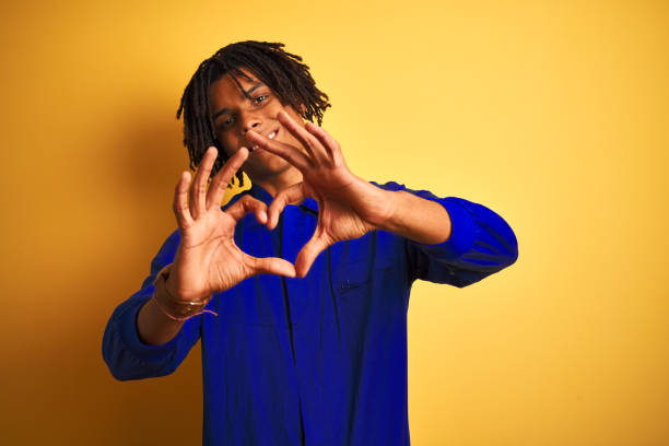 istock Afro worker man with dreadlocks wearing mechanic uniform over isolated yellow background smiling in love doing heart symbol shape with hands. Romantic concept. 1187193028
