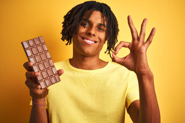 istock Afro american man with dreadlocks eating chocolate bar over isolated yellow background doing ok sign with fingers, excellent symbol 1187193218