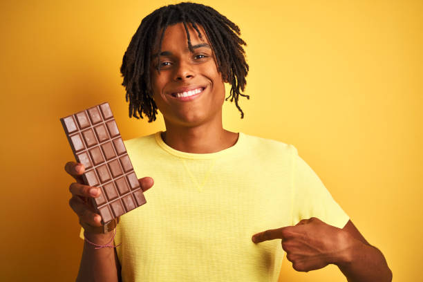 istock Afro american man with dreadlocks eating chocolate bar over isolated yellow background with surprise face pointing finger to himself 1187193264