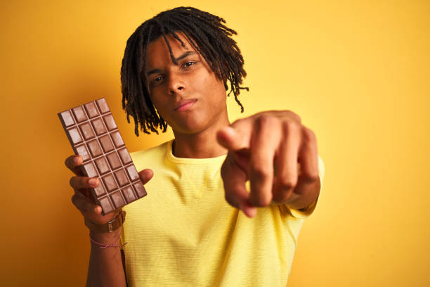 istock Afro american man with dreadlocks eating chocolate bar over isolated yellow background pointing with finger to the camera and to you, hand sign, positive and confident gesture from the front 1187193372