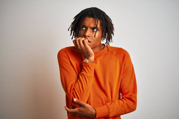 istock Afro american man with dreadlocks wearing orange sweater over isolated white background looking stressed and nervous with hands on mouth biting nails. Anxiety problem. 1187194080