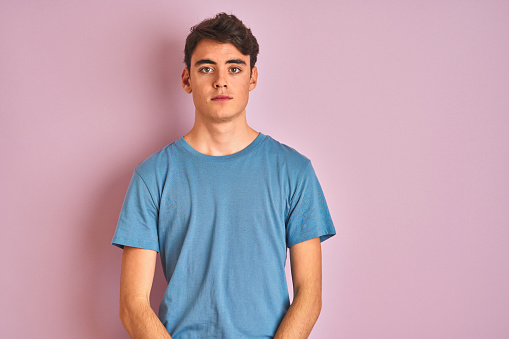 Teenager boy wearing casual t-shirt standing over blue isolated background with serious expression on face. Simple and natural looking at the camera.
