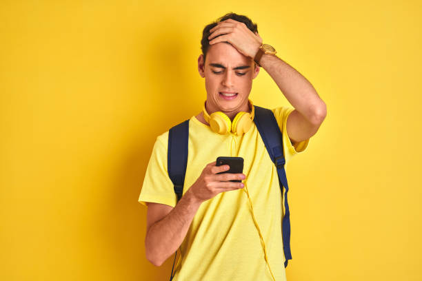 garçon d'adolescent utilisant des écouteurs et utilisant le smartphone au-dessus du fond isolé stressé avec la main sur la tête, choqué avec la honte et le visage de surprise, fâché et frustré. peur et contrarié par erreur. - frustration male beauty one person problems photos et images de collection