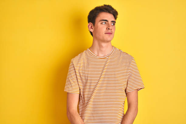 teenager junge trägt gelbes t-shirt über isolierten hintergrund lächelnd blickend zur seite und starrt weg denken. - mannered stock-fotos und bilder