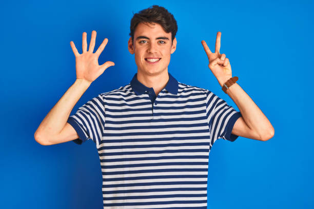 teenager junge trägt lässige t-shirt stehen über blauen isolierten hintergrund zeigt und zeigt mit den fingern nummer sieben, während lächelnd zuversichtlich und glücklich. - beautiful one person men male stock-fotos und bilder