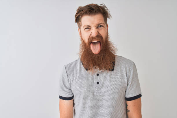 istock Young redhead irish man wearing grey polo standing over isolated white background sticking tongue out happy with funny expression. Emotion concept. 1187194906