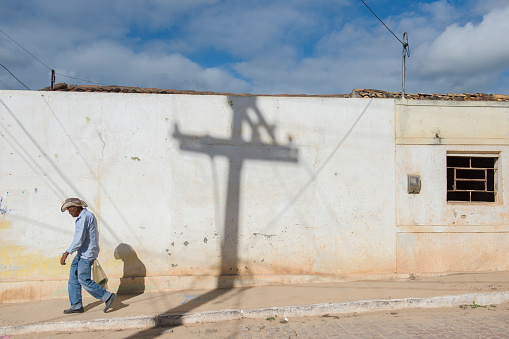 Buique, Pernambuco, Brazil - June 15, 2016: Senior Afro Brazilian cowboy walking on the sidewalk, carrying a shopping bag during a sunny day. The hinterlands of northeast Brazil are the poorest area of the country, with a massive number of families living under the standard rates of Brazilians social life conditions.