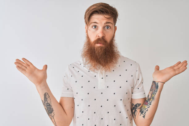 Young redhead irish man wearing polo standing over isolated white background clueless and confused expression with arms and hands raised. Doubt concept. Young redhead irish man wearing polo standing over isolated white background clueless and confused expression with arms and hands raised. Doubt concept. shoulder tattoo designs for men stock pictures, royalty-free photos & images
