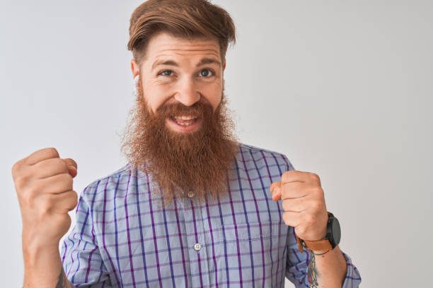 redhead 아일랜드 남자는 고립 된 흰색 배경에 무선 이어폰을 사용하여 음악을 듣고 매우 행복하고 팔을 들고, 미소와 성공을 위해 비명을 지르는 우승자 제스처를하고 흥분. 축 하 개념입니다. - irish culture audio 뉴스 사진 이미지