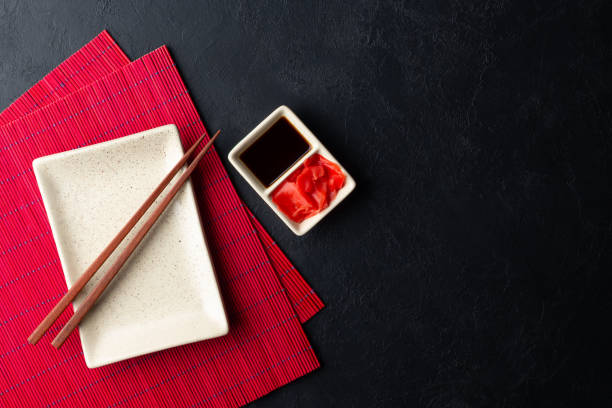 istock Sushi chopsticks, soy sauce, ginger, red bamboo mat and empty plate on black background. 1187197694