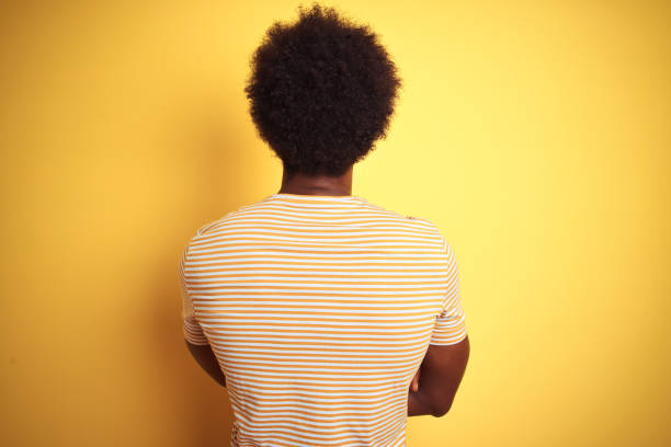 homem americano com cabelo afro que desgasta o t-shirt listrado que está sobre o fundo amarelo isolado que está para trás olhando afastado com braços cruzados - back to the wall - fotografias e filmes do acervo