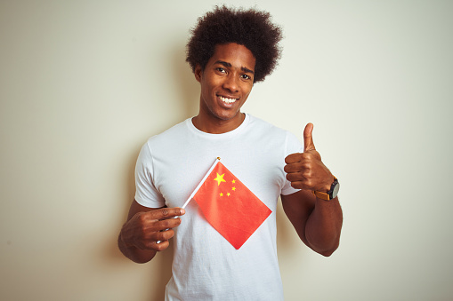 Young afro american man holding China Chinese flag standing over isolated white background happy with big smile doing ok sign, thumb up with fingers, excellent sign