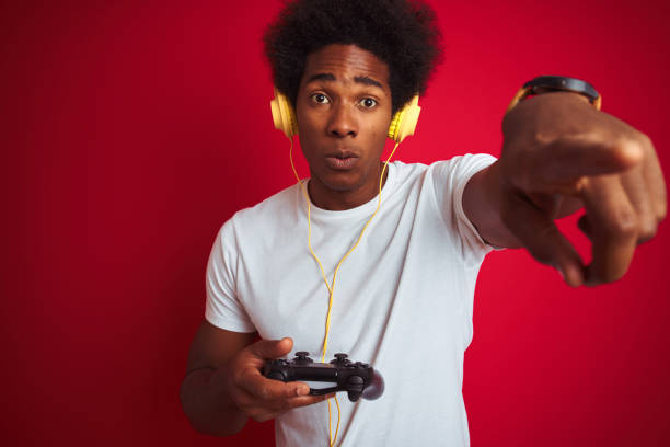 istock Afro gamer man playing video game using joystick headphones over isolated red background pointing with finger to the camera and to you, hand sign, positive and confident gesture from the front 1187198722