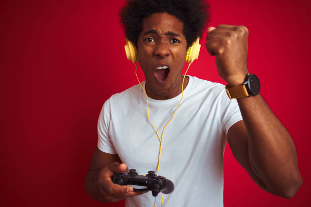 istock Afro gamer man playing video game using joystick headphones over isolated red background annoyed and frustrated shouting with anger, crazy and yelling with raised hand, anger concept 1187198736