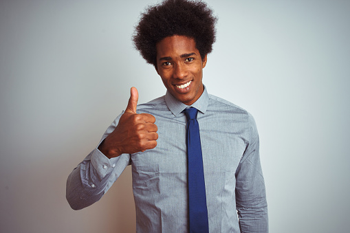 American business man with afro hair wearing shirt and tie over isolated white background doing happy thumbs up gesture with hand. Approving expression looking at the camera showing success.