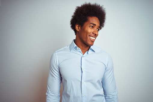 Young african american man with afro hair wearing elegant shirt over isolated white background looking away to side with smile on face, natural expression. Laughing confident.