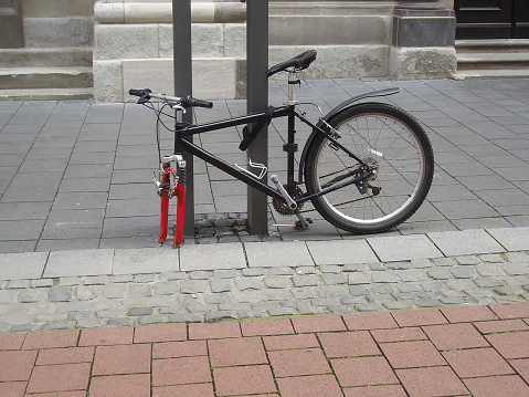 A bicycle fastened to a post stands on the street. One wheel stolen from a bicycle.