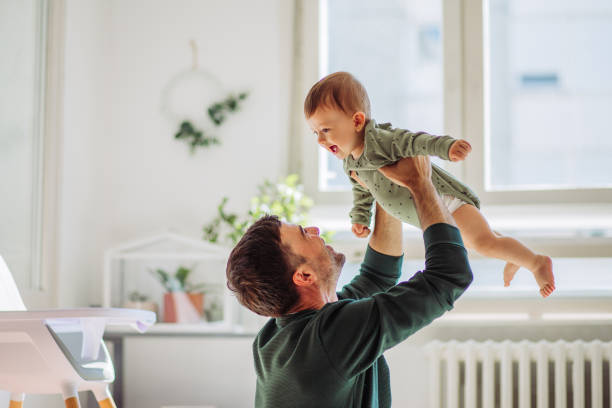 Fun time Father carrying baby son and they playing around in living room genderblend stock pictures, royalty-free photos & images