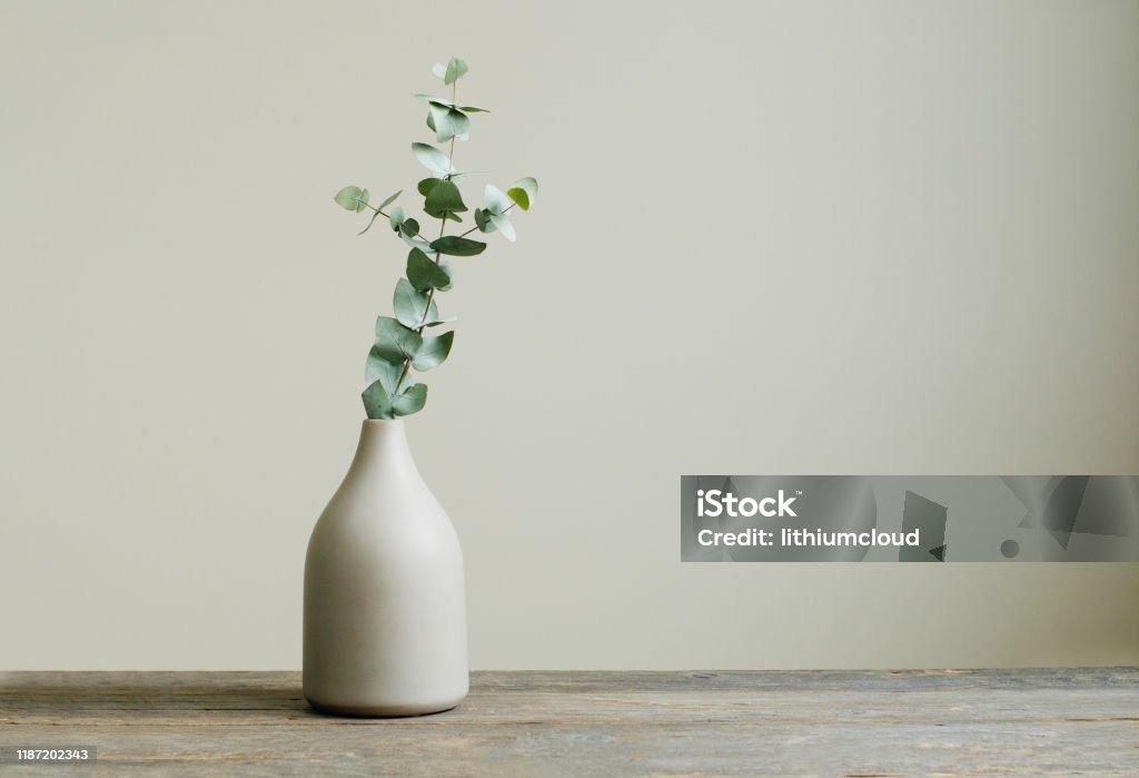 Eucalyptus branch in a vase on the rustic wooden table Detail of contemporary cozy interior. Eucalyptus branch in a vase on the rustic wooden table. Blank space for text on the wall. Vase Stock Photo