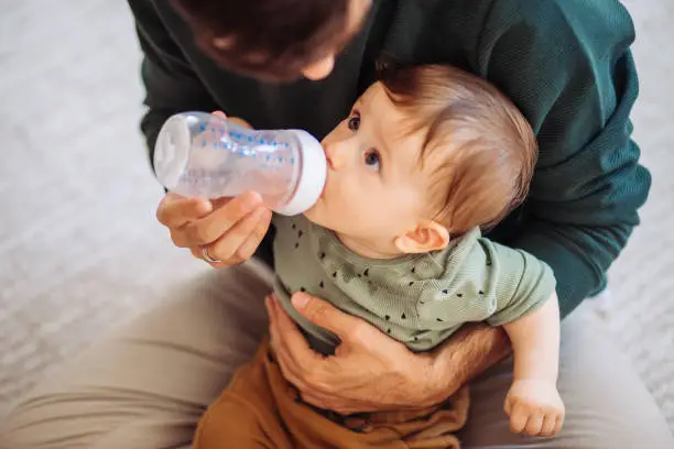 Father and son sitting on floor, baby boy drinking water from baby bottle