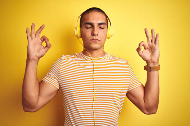 istock Young handsome man using headphones over yellow isolated background relax and smiling with eyes closed doing meditation gesture with fingers. Yoga concept. 1187204314