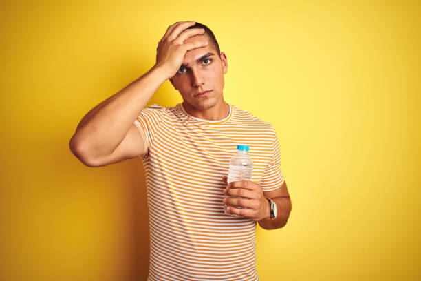 istock Young handsome man holding plastic water bottle over yellow isolated background stressed with hand on head, shocked with shame and surprise face, angry and frustrated. Fear and upset for mistake. 1187204439