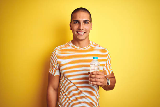 istock Young handsome man holding plastic water bottle over yellow isolated background with a happy face standing and smiling with a confident smile showing teeth 1187204454